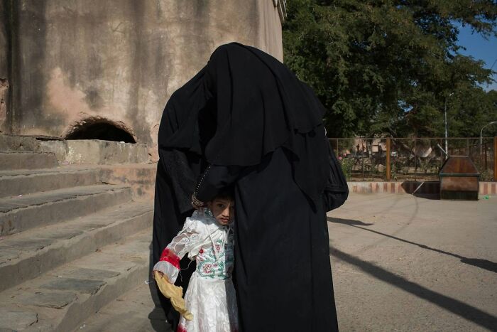A street photographer captures a serendipitous moment of a woman in a black abaya with a child peeking out in everyday life.
