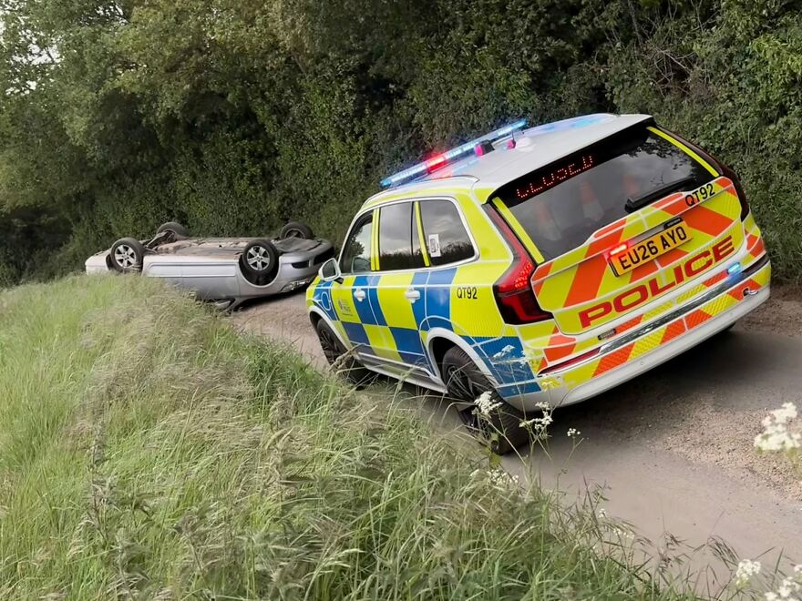 A police car attending an overturned vehicle on a rural road, a rough day behind the wheel.