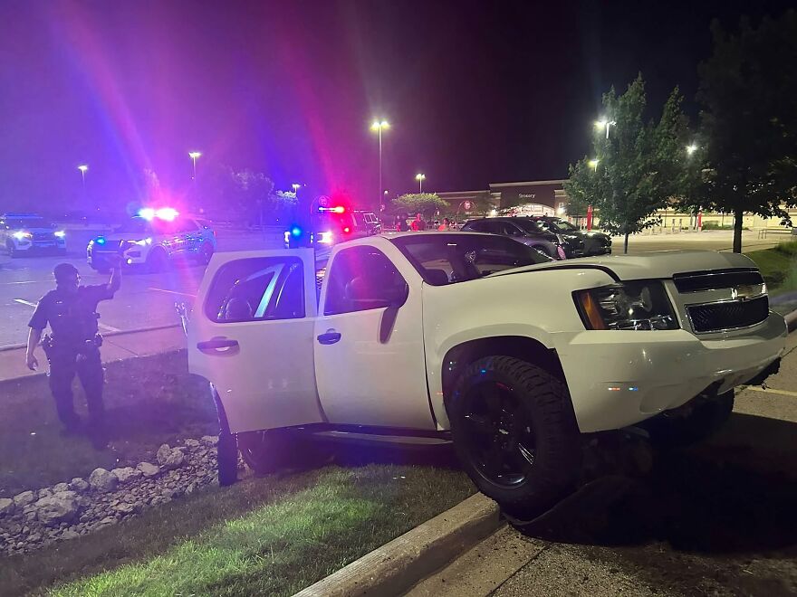 A white SUV in a ditch next to a parking lot at night, police lights flashing, a rough day behind the wheel.