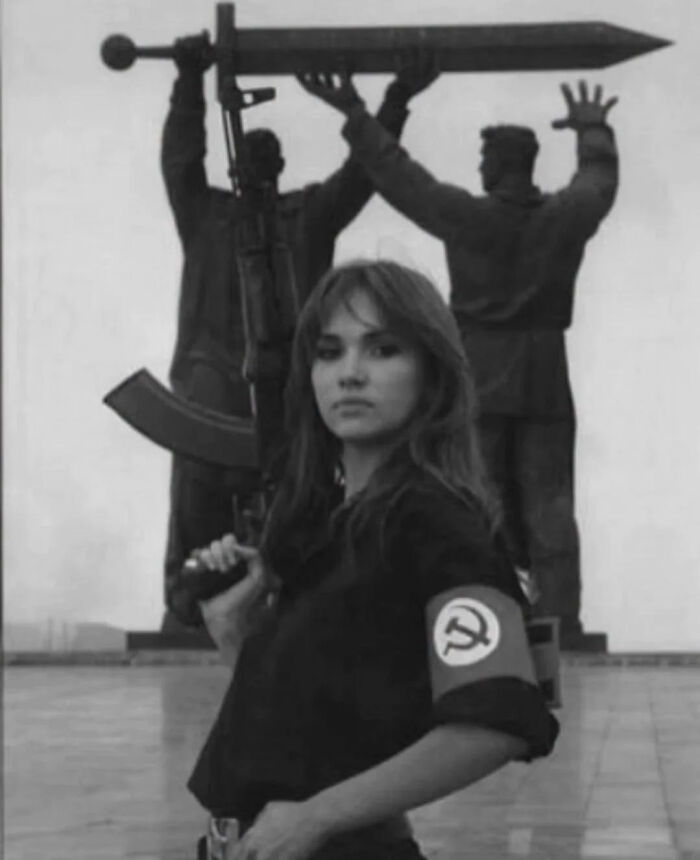 A woman in a dark shirt with a hammer and sickle armband holding a rifle, representing overlooked women in history.