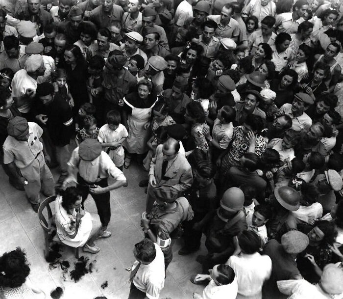 A woman has her head shaved in front of a crowd, a scene depicting overlooked women in history.