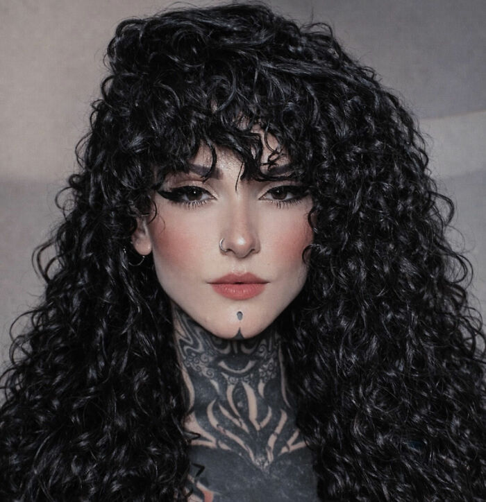 Close-up of a goth influencer with curly dark hair, facial piercings, and neck tattoos. Close-up of a goth influencer with curly dark hair, facial piercings, and neck tattoos.