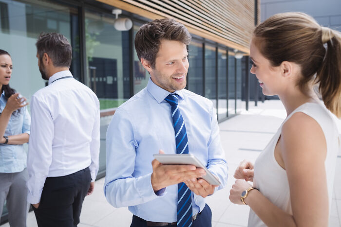 Man in a blue shirt and striped tie, holding a tablet and talking to a woman, in an image about jobs guys have.