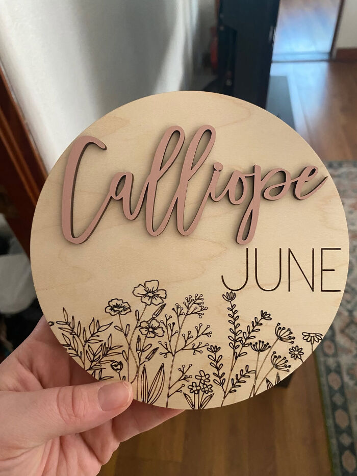 A wooden circle with the baby name Calliope June, decorated with wildflowers. This showcases unique baby names.