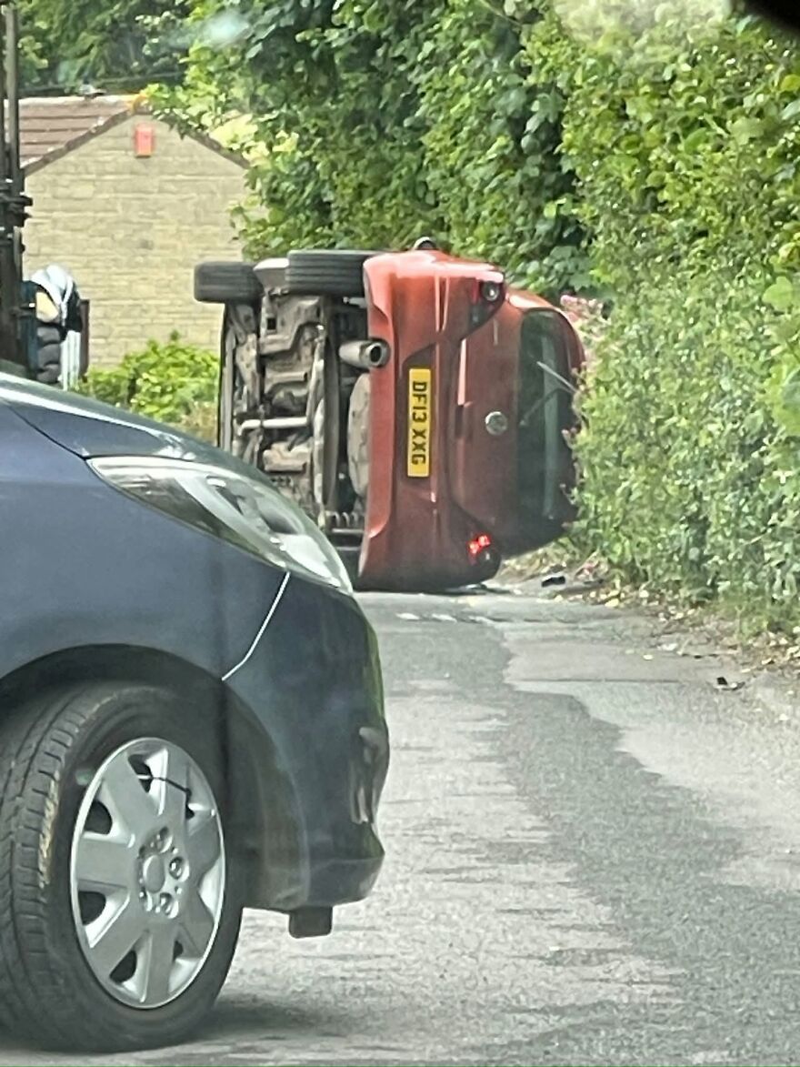 A red car overturned on its side on a narrow road, demonstrating a rough day behind the wheel.