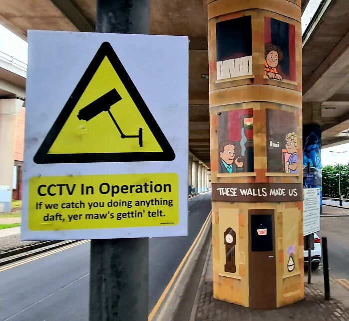 An absurd CCTV warning sign with a humorous Scottish phrase, next to a painted building column.