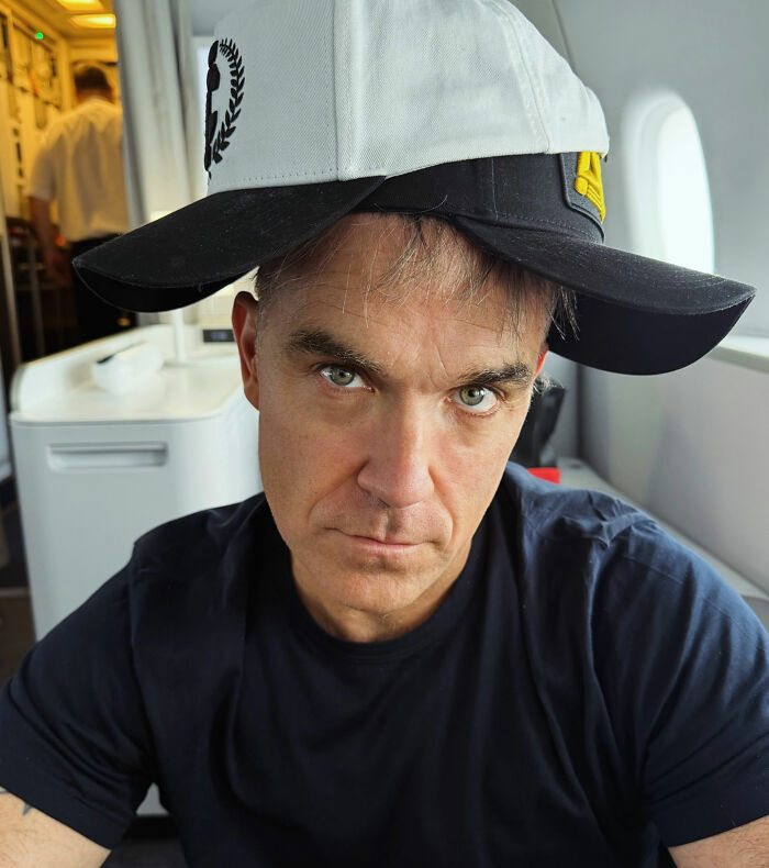 Robbie Williams wearing two hats, looking serious, after the World Cup moment with white substance on his mic. Robbie Williams wearing two hats, looking serious, after the World Cup moment with white substance on his mic.