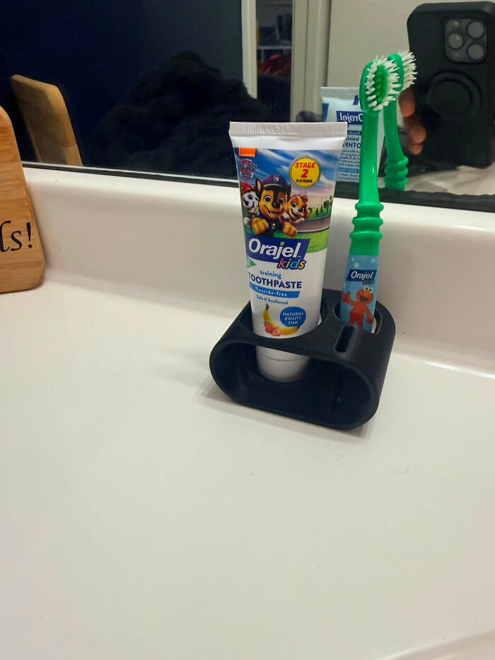 A practical 3D printer creation: a custom holder for kids' toothpaste and toothbrush on a sink counter.