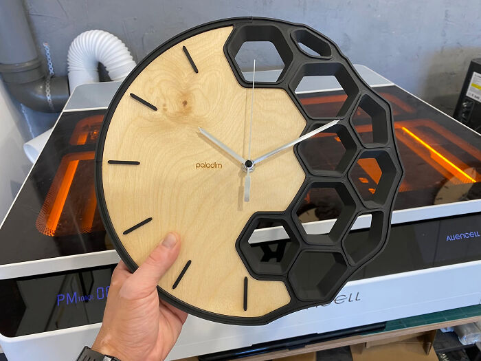 A unique wooden and honeycomb-patterned wall clock, a cool thing created with a 3D printer, held by a hand.