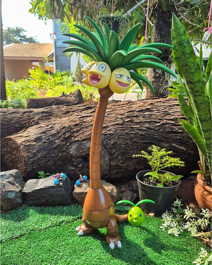 A large 3D printed Exeggutor Pokémon figure with multiple heads and palm tree leaves, standing in a garden setting.