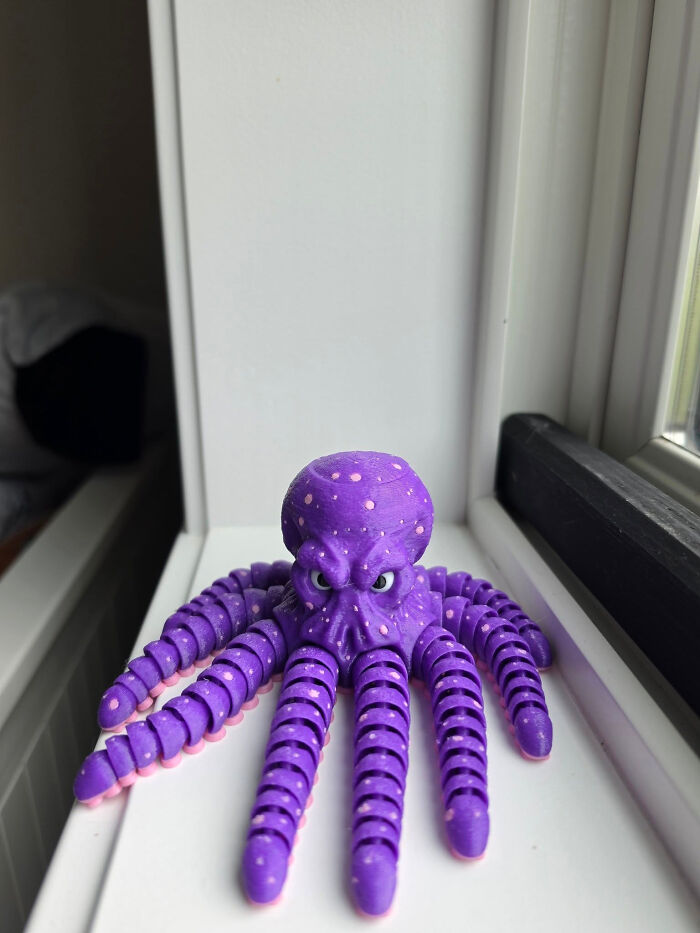 A purple 3D printed octopus with pink suckers on its tentacles and small white dots, sitting on a white surface.