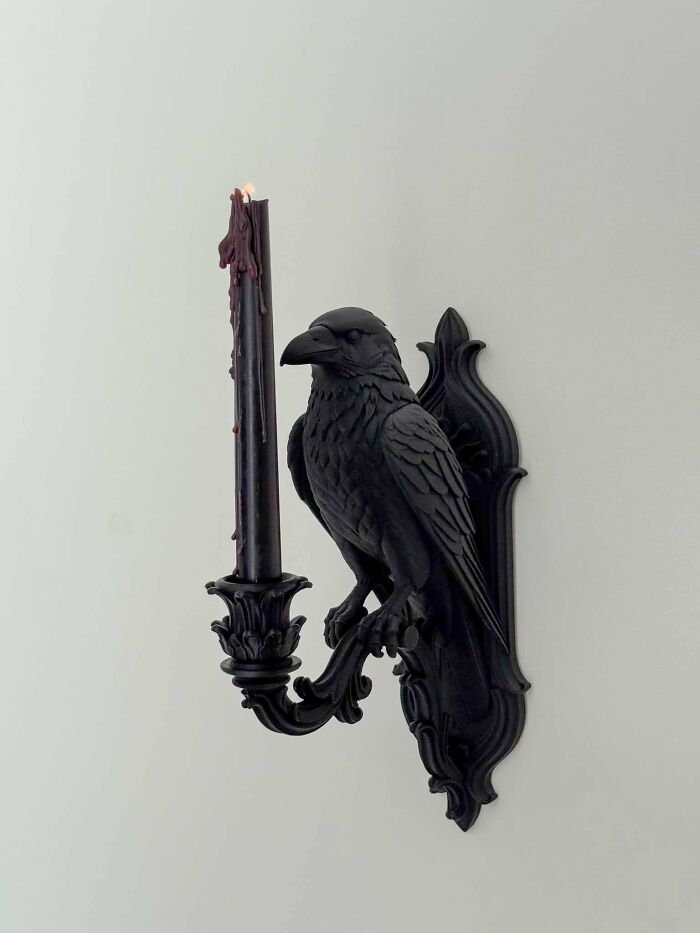 A black raven-shaped sconce holding a burning candle, demonstrating a cool and useful item created with a 3D printer.
