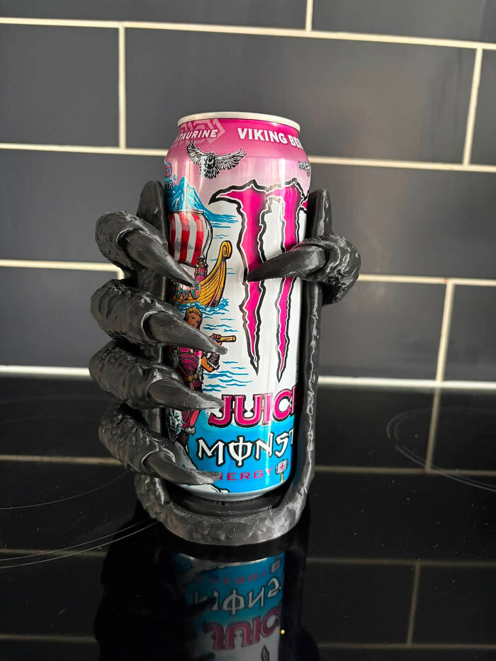 A Monster Energy drink can held by a fierce, clawed holder, a cool thing created with a 3D printer.