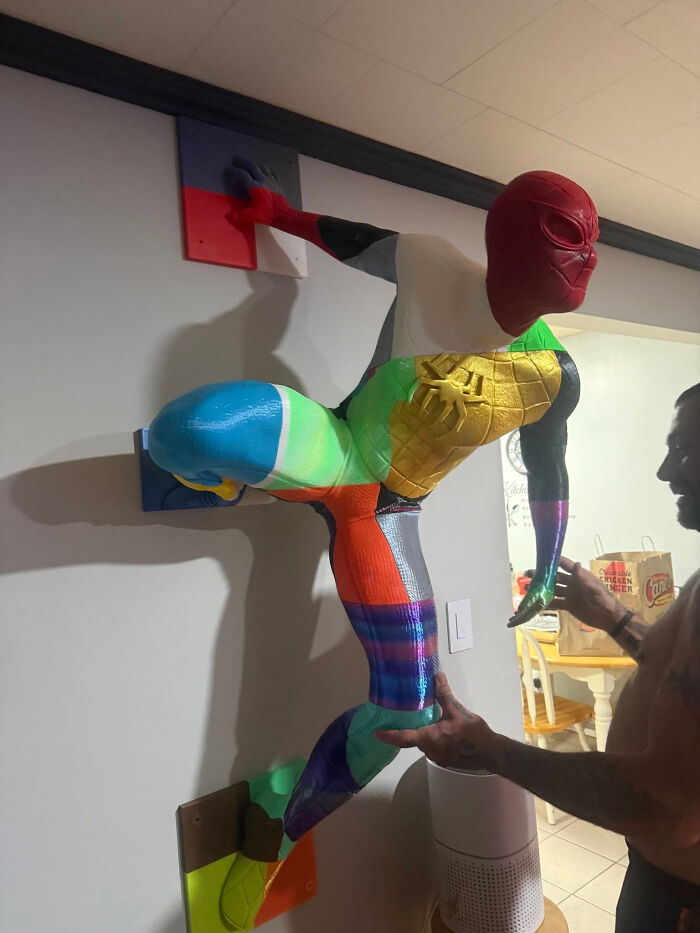 A vibrant, multi-colored Spider-Man figure created with a 3D printer, scaling a wall.