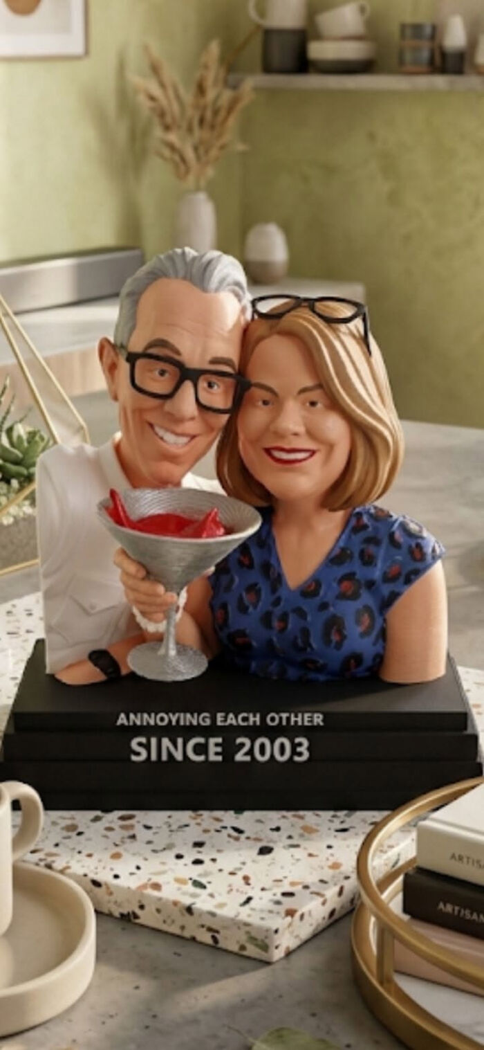 A humorous 3D printer creation of a couple's bobblehead, celebrating their anniversary, with a sign Annoying Each Other Since 2003.