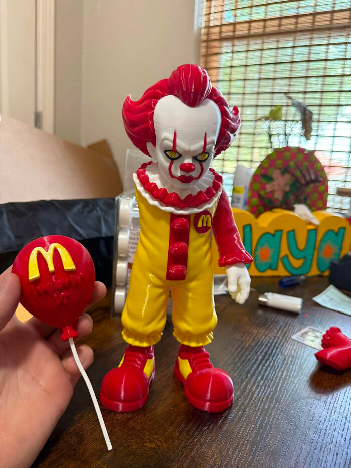 A frightening 3D printer creation of Pennywise the clown in Ronald McDonald attire, holding a McDonald's balloon.