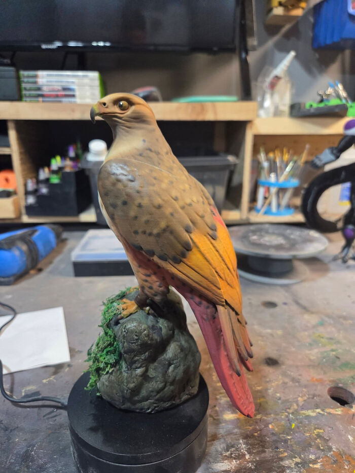 A detailed 3D printer creation of a colorful hawk perched on a mossy rock.