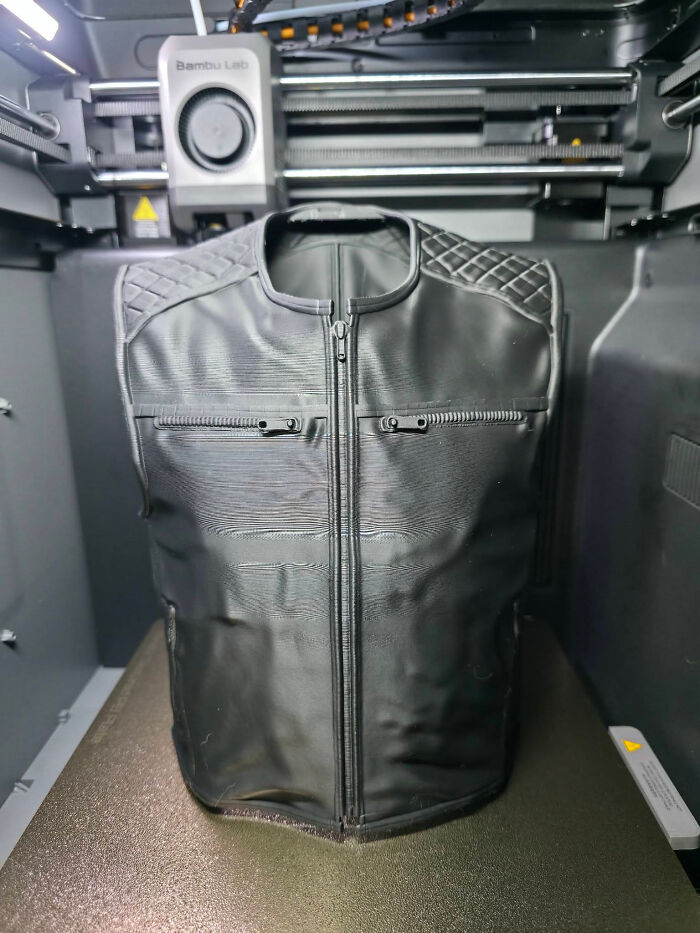 A black leather-look vest being created inside a 3D printer.