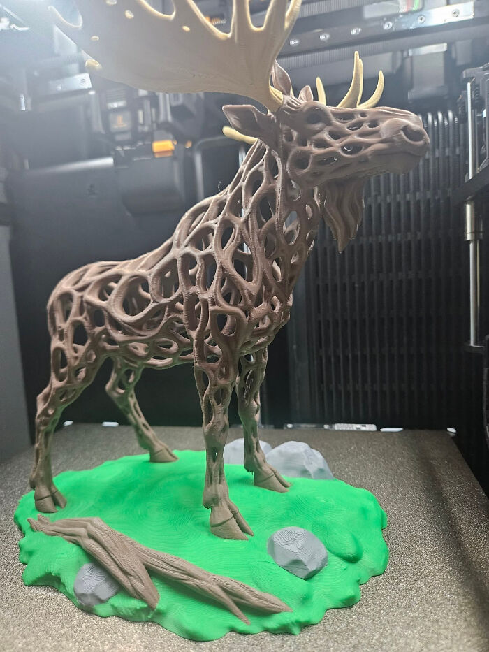 An elaborate brown 3D printed moose sculpture with a hollow, web-like body, standing on a green base, showcasing things created with a 3D printer.