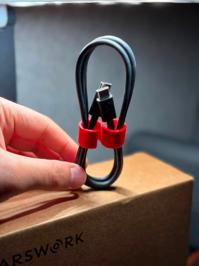A hand holding a coiled cable secured with a red 3D printed cable tie. A useful 3D printed item.