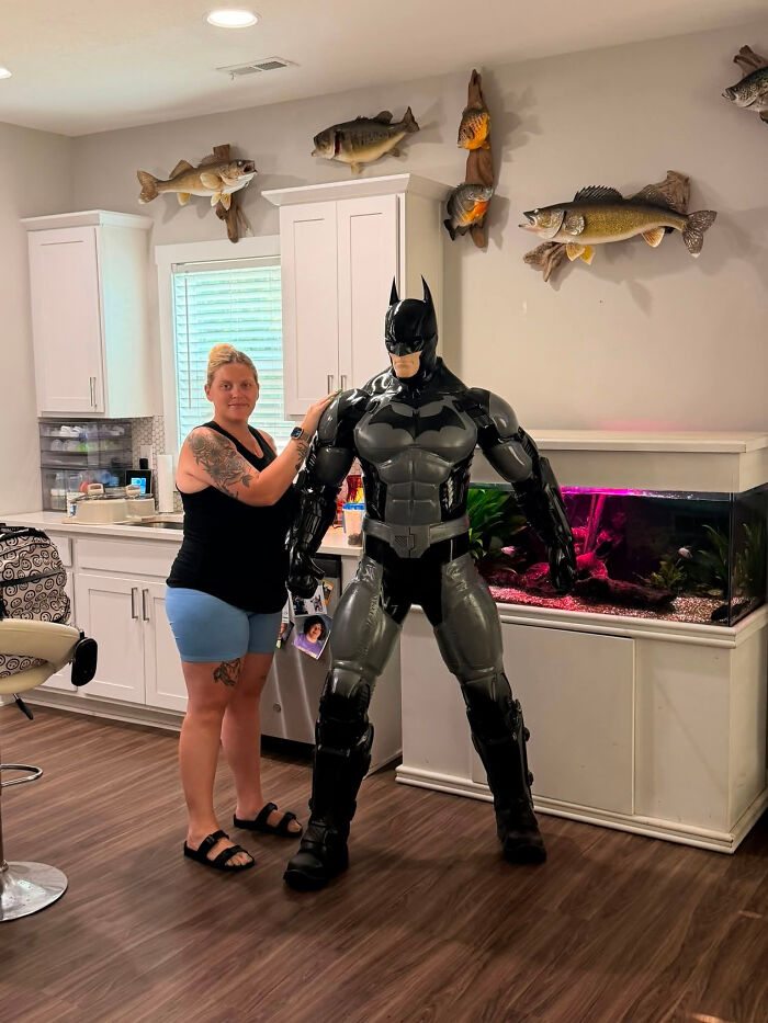 A woman posing with a large, realistic 3D printer creation of Batman in a living room.