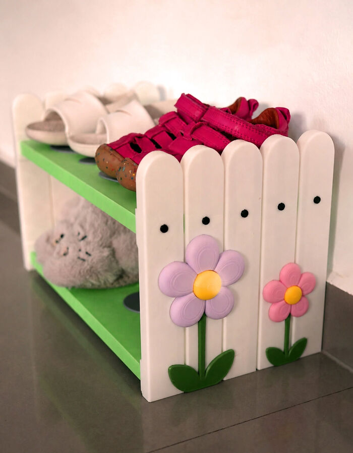 A white and green 3D printer shoe rack with flower decorations holding various shoes and slippers.