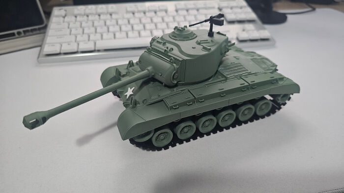 A military-green 3D printed tank model on a white surface with a keyboard in the background, a cool thing created with a 3D printer.