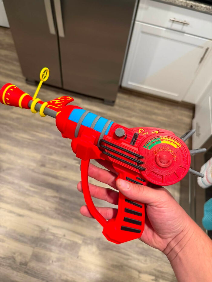 A person holding a vibrant red 3D printer creation, a ray gun with yellow, blue, and black accents.