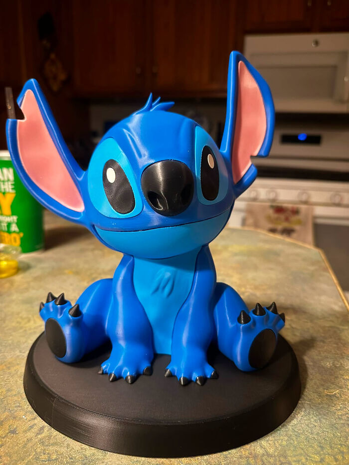 A blue Stitch figure, a cool and useful creation made with a 3D printer, sitting on a black base.