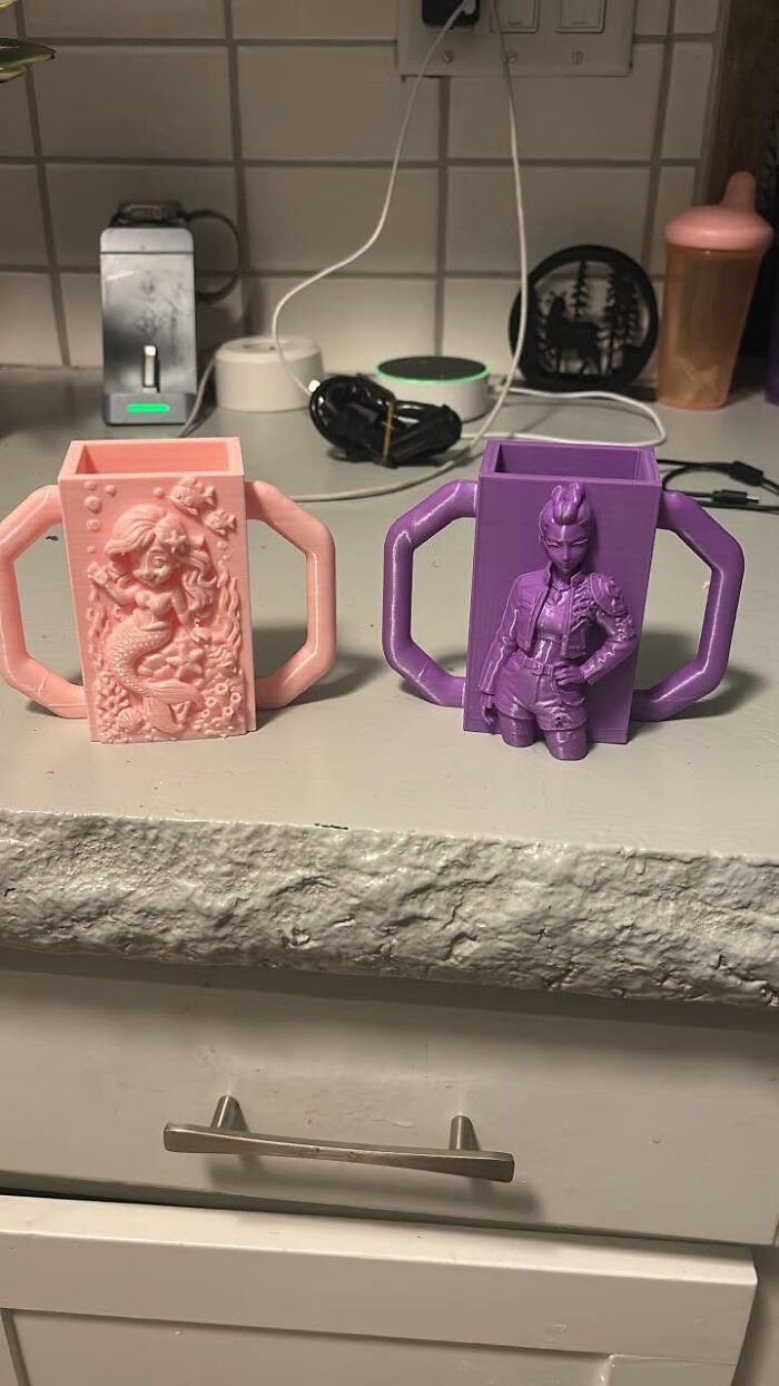 Two custom 3D printer mugs, one pink with a mermaid and one purple with a superheroine, cool and useful.