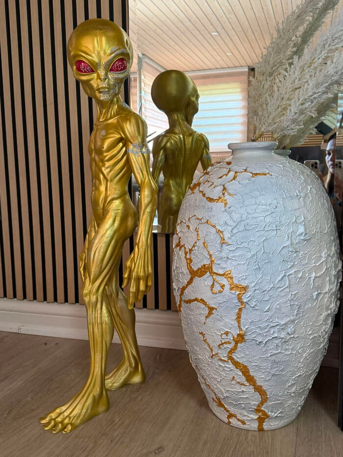 A tall golden alien figure standing next to a textured white and gold vase, a cool 3D printer creation.