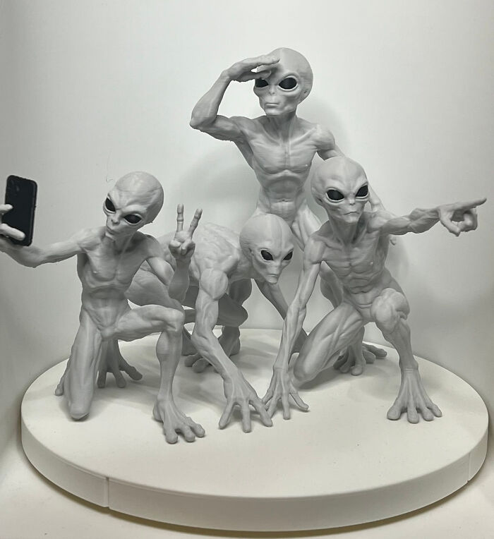 A humorous 3D printer creation of four gray aliens striking different poses, one taking a selfie.