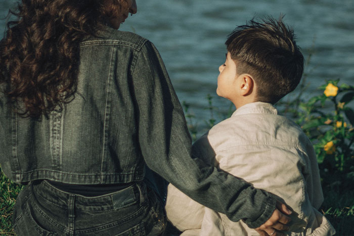 A parent with an arm around a child, looking at the water, considering the impact of unfortunate names.