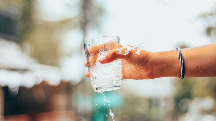 A hand spills water from a glass, illustrating a minor 'accident' or 'prank' scenario.