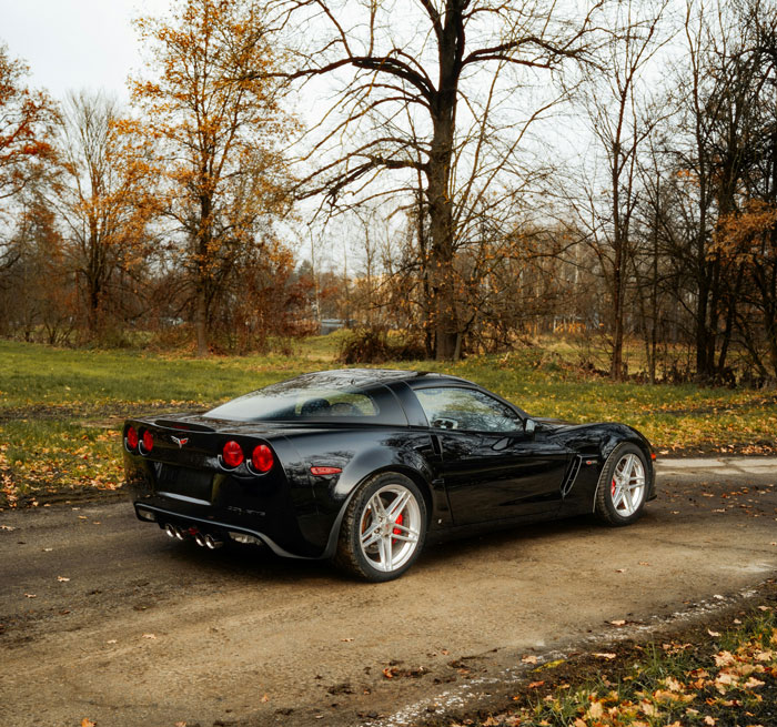 A sleek black sports car, surprisingly affordable, parked on a dirt road amidst autumn trees.