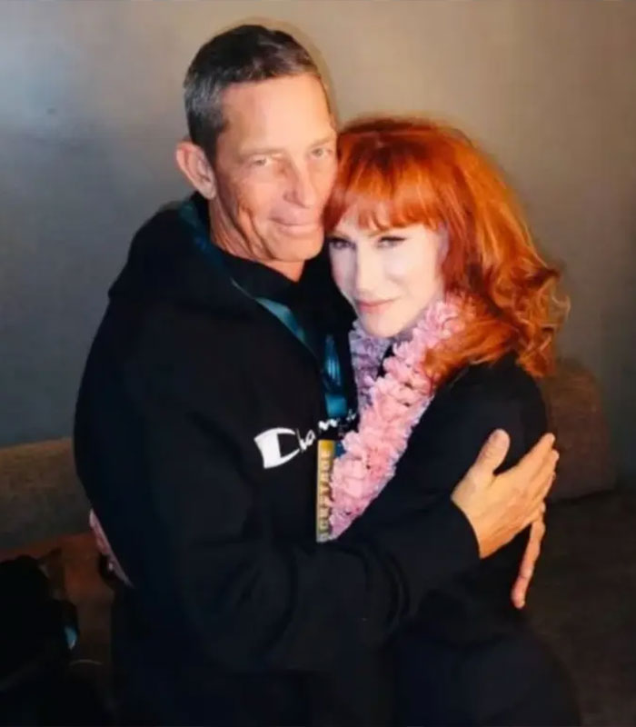 Star in her 60s, a woman with red hair and pink lei, embraces a man in a black hoodie, revealing their relationship. Star in her 60s, a woman with red hair and pink lei, embraces a man in a black hoodie, revealing their relationship.
