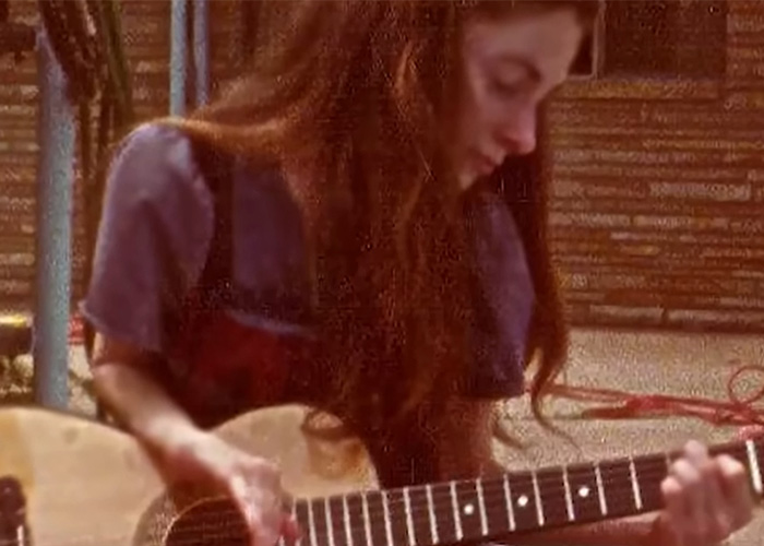 A young polio survivor with long brown hair plays an acoustic guitar, finding joy despite living in an iron lung.