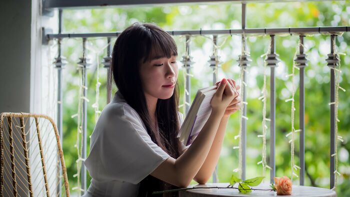 Woman reading a book on a balcony, judging dating scenarios by their red, green, and beige flags.