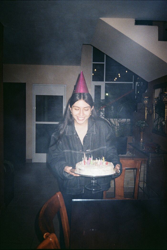 A young woman wearing a party hat, holding a birthday cake with lit candles, celebrating a special occasion with interesting facts.