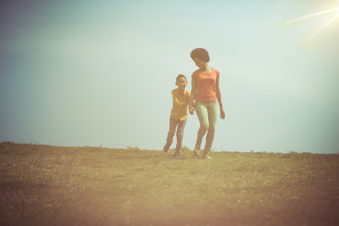 A mother and child running across a sunlit grassy field, hinting at mysterious things happening.
