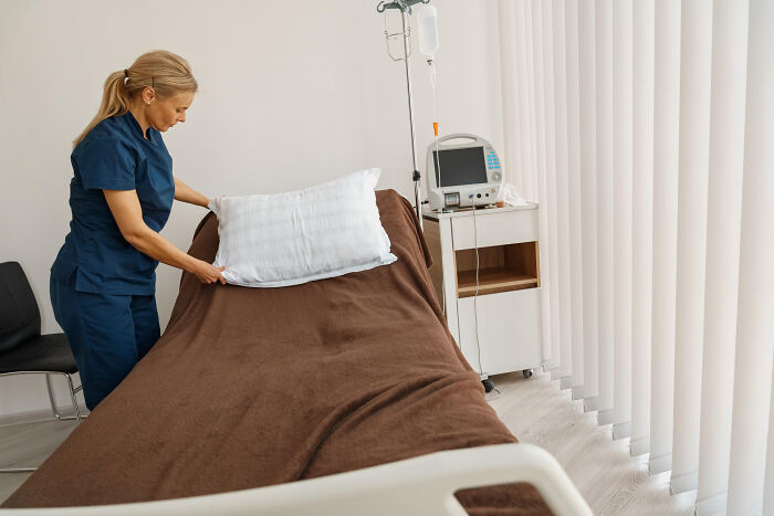 A nurse in blue scrubs makes a bed in a hospital room, highlighting truths about the medical industry.