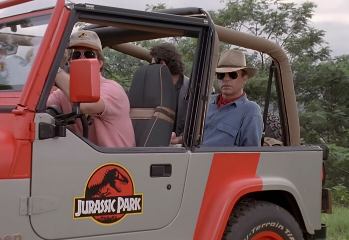 Sam Neill as Dr. Alan Grant in a Jurassic Park jeep with other characters. Sam Neill as Dr. Alan Grant in a Jurassic Park jeep with other characters.