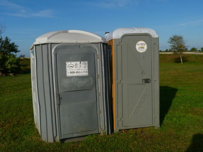 Two portable toilets in a grassy field under a blue sky, representing a public horror story scenario.