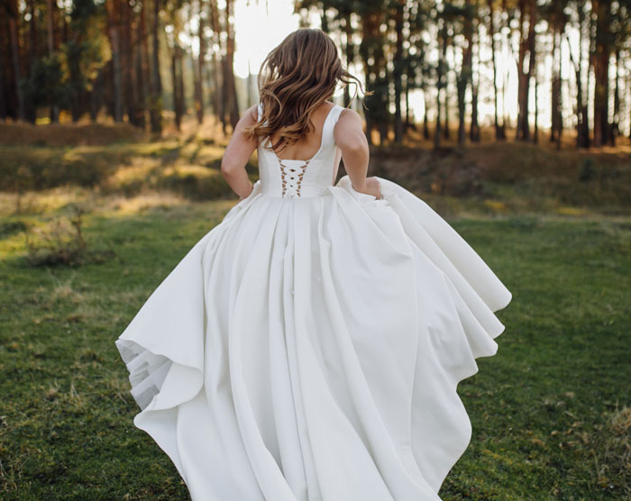 A bride in a white wedding dress running through a forest, back to the camera. The bride forbids brother from wearing a dress. A bride in a white wedding dress running through a forest, back to the camera. The bride forbids brother from wearing a dress.