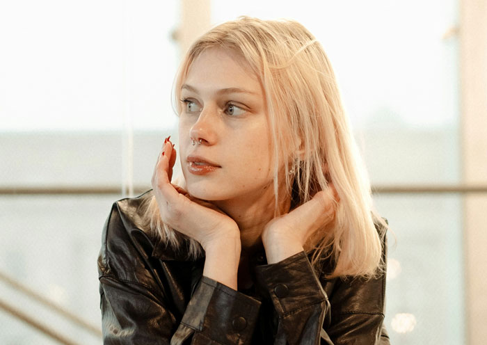 A young woman with blonde hair looking pensive, perhaps considering a clever comeback or reaction.