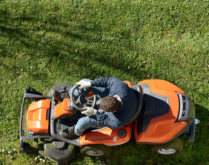 An overhead view of a man on a ride-on lawnmower, highlighting dumb warning labels.
