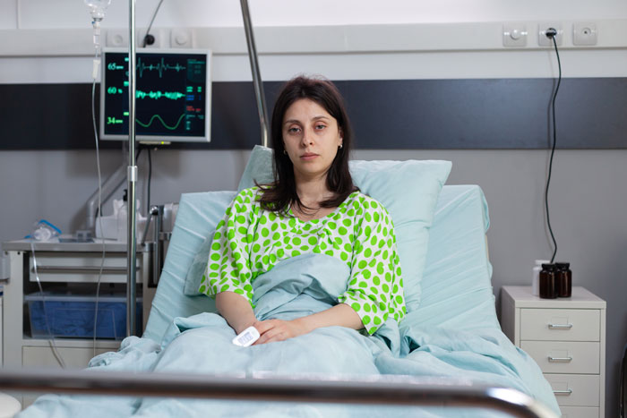 Female patient sits on a hospital bed with medical equipment in the background, showing the hidden side of hospitals.