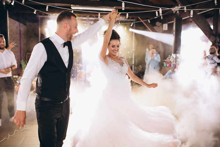 A happy bride and groom dancing together amidst smoke and spotlights at their wedding.
