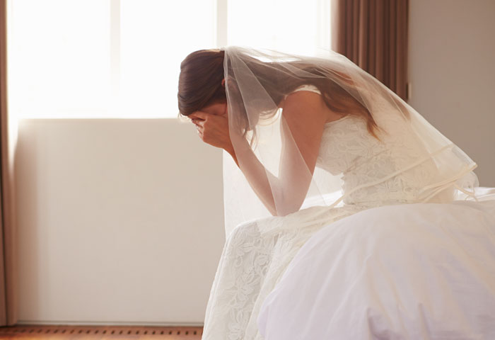 A bride sitting with her head in her hands, distraught, perhaps due to circumstances requiring a divorce lawyer.