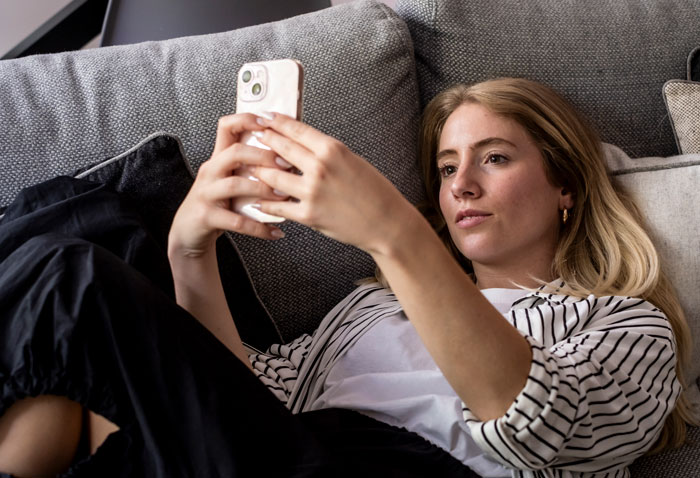 A young woman lounging on a gray couch, focused on her phone, illustrating hard truths women learned.